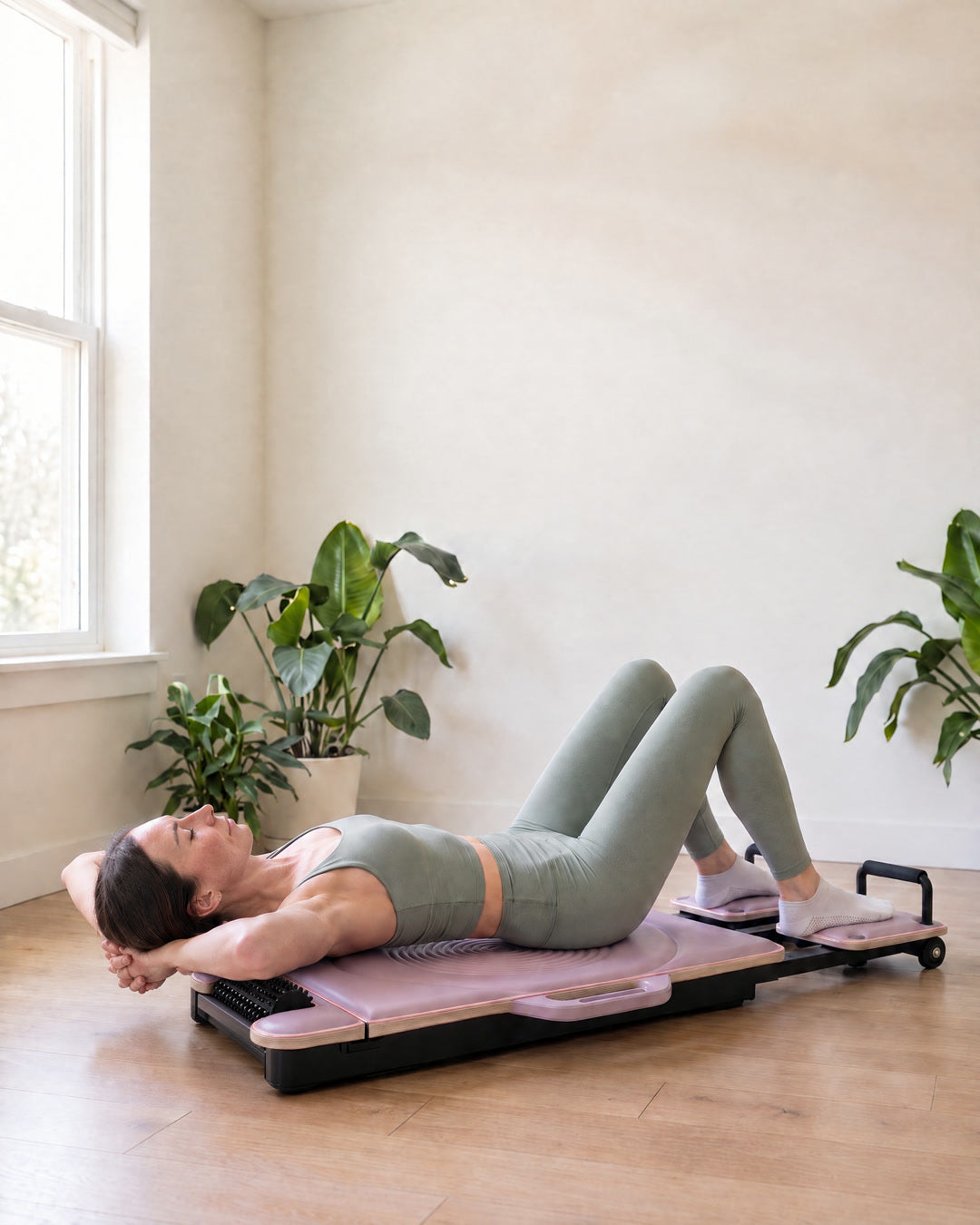 A woman in a light green sports set lying on her back on the lilac DROP-IN board, her upper back resting on its built-in spiked roller, hands behind her head.